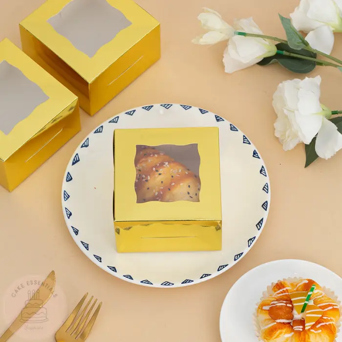 A set of gold bakery gift boxes measuring 4x4x2.5 inches, featuring a clear window on the top. Ideal for packaging cupcakes, pastries, and small baked goods elegantly.